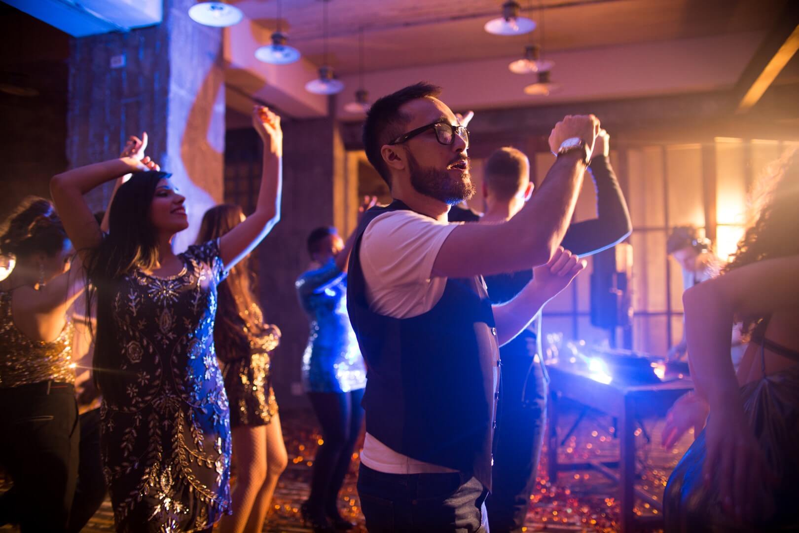 Crowd of trendy  people dancing in nightclub with golden confetti flying around, focus on Asian man dancing in center enjoying party